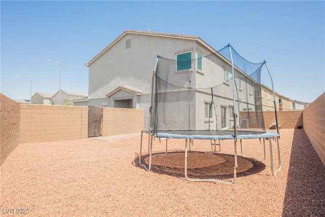 7002 Fossil Rim St, North Las Vegas, NV 89084 - back of house featuring a trampoline, a fenced backyard, and stucco siding