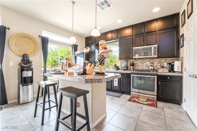 9704 Morgan Creek Ct, Las Vegas, NV 89141 - kitchen with stainless steel appliances, a center island, tasteful backsplash, a kitchen bar, and light tile patterned floors