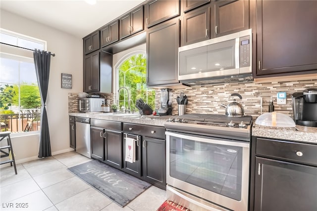 9704 Morgan Creek Ct, Las Vegas, NV 89141 - kitchen with stainless steel appliances, a sink, tasteful backsplash, light tile patterned floors, and dark brown cabinets