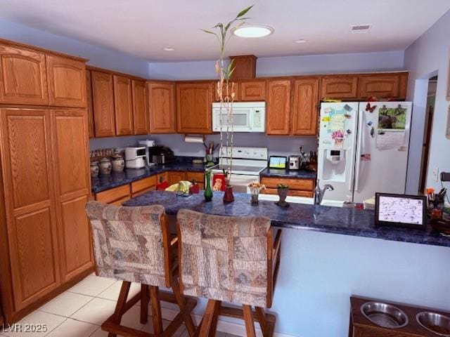 3368 Saddleback Ct, Las Vegas, NV 89121 - kitchen featuring white appliances, brown cabinetry, light tile patterned flooring, a breakfast bar, and a sink