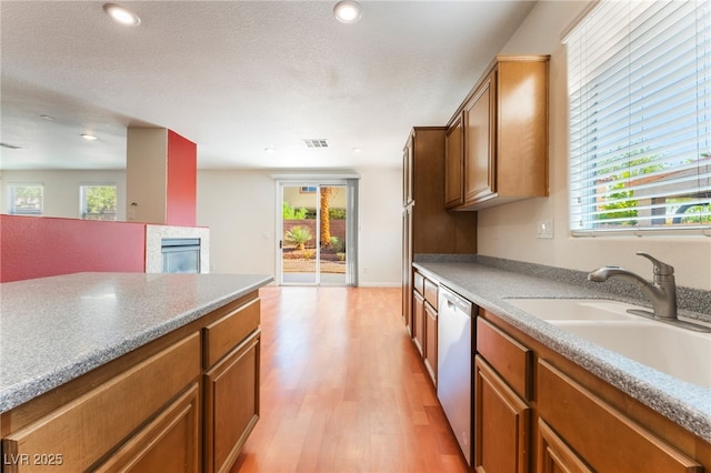 908 Cypress Gold Ct, North Las Vegas, NV 89031 - kitchen with dishwasher, light wood-style flooring, a glass covered fireplace, a sink, and plenty of natural light
