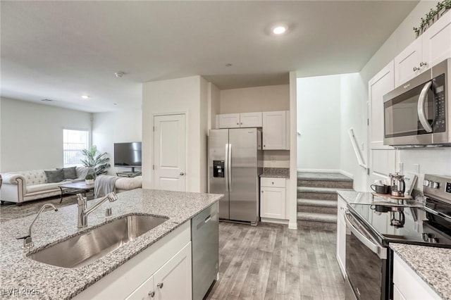 12728 Feathersong St, Henderson, NV 89044 - kitchen featuring appliances with stainless steel finishes, a sink, light wood-type flooring, white cabinets, and light stone counters