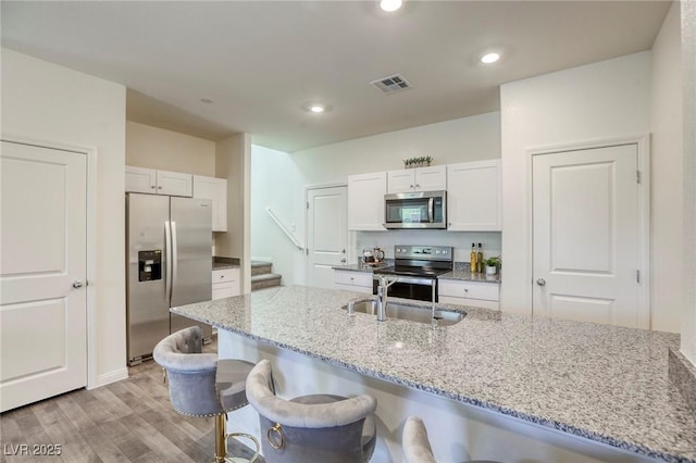 12728 Feathersong St, Henderson, NV 89044 - kitchen with stainless steel appliances, a sink, light wood-type flooring, a breakfast bar area, and light stone counters