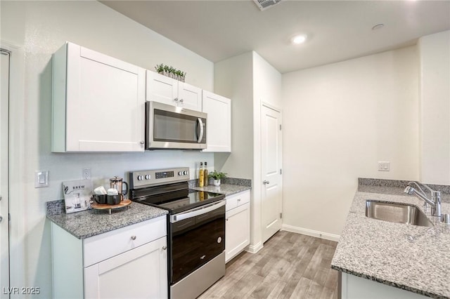 12728 Feathersong St, Henderson, NV 89044 - kitchen featuring stainless steel appliances, light wood-style flooring, a sink, baseboards, and white cabinets