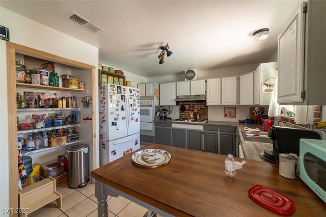 6432 Aberdeen Ln, Las Vegas, NV 89107 - kitchen with white appliances, under cabinet range hood, light tile patterned flooring, a warming drawer, and white cabinetry