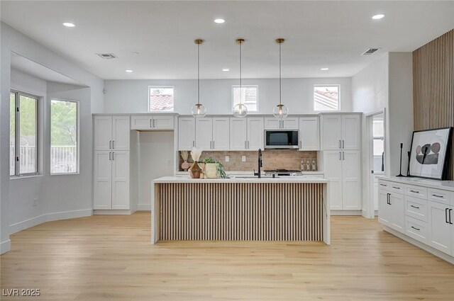 2353 Lauren Dr, Las Vegas, NV 89134 - kitchen featuring stainless steel microwave, light wood-style floors, decorative backsplash, a center island with sink, and hanging light fixtures