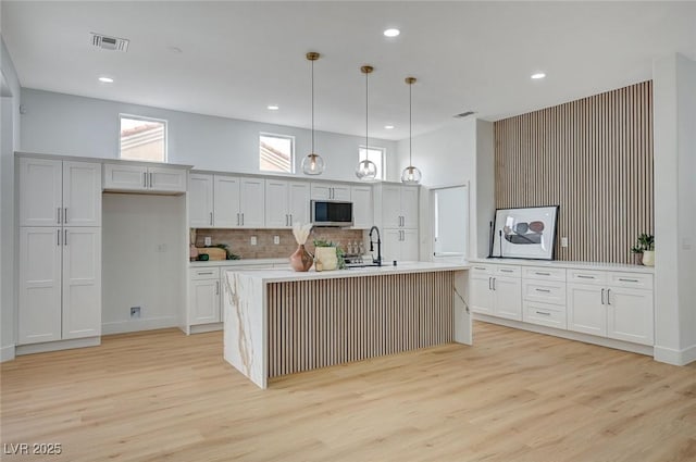 2353 Lauren Dr, Las Vegas, NV 89134 - kitchen featuring stainless steel microwave, light wood-style floors, hanging light fixtures, light countertops, and decorative backsplash