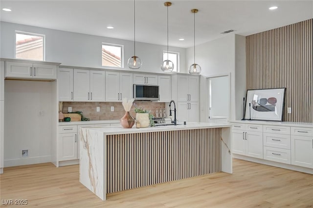 2353 Lauren Dr, Las Vegas, NV 89134 - kitchen with stainless steel microwave, light wood-type flooring, backsplash, a center island with sink, and recessed lighting