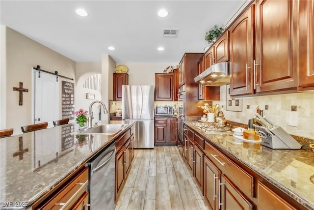 10420 Loma Portal Ave, Las Vegas, NV 89166 - kitchen with under cabinet range hood, stainless steel appliances, a sink, a barn door, and dark stone countertops