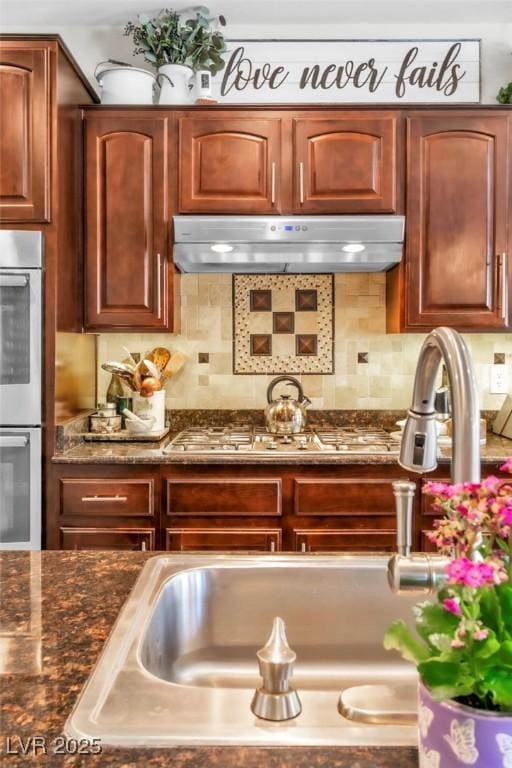 10420 Loma Portal Ave, Las Vegas, NV 89166 - kitchen with stainless steel double oven, under cabinet range hood, decorative backsplash, and dark stone counters