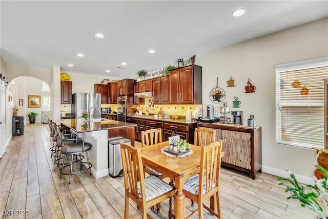 10420 Loma Portal Ave, Las Vegas, NV 89166 - kitchen featuring arched walkways, light wood-type flooring, appliances with stainless steel finishes, recessed lighting, and a kitchen breakfast bar