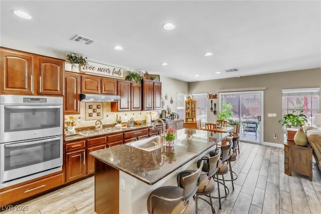 10420 Loma Portal Ave, Las Vegas, NV 89166 - kitchen with double oven, gas cooktop, under cabinet range hood, dark stone countertops, and a sink