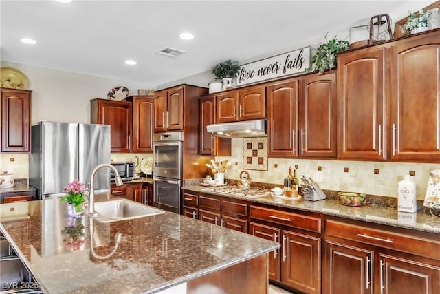 10420 Loma Portal Ave, Las Vegas, NV 89166 - kitchen with stainless steel appliances, under cabinet range hood, a sink, dark stone countertops, and a center island with sink