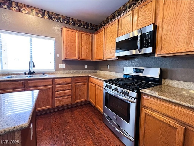 3412 Catherine Mermet Ave, North Las Vegas, NV 89081 - kitchen featuring appliances with stainless steel finishes, a sink, dark wood finished floors, and brown cabinetry