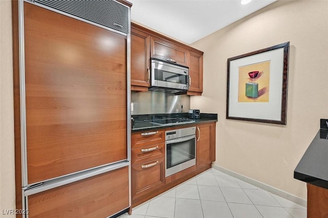 135 E Harmon Ave Unit 1401, Las Vegas, NV 89109 - kitchen featuring stainless steel appliances, dark countertops, brown cabinetry, baseboards, and light tile patterned floors