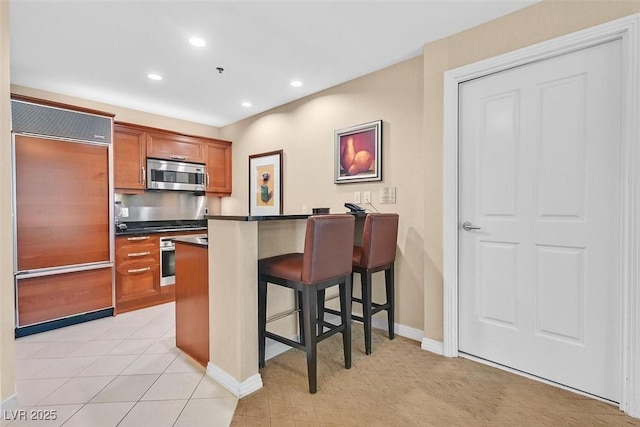 135 E Harmon Ave Unit 1401, Las Vegas, NV 89109 - kitchen featuring appliances with stainless steel finishes, brown cabinets, dark countertops, a kitchen breakfast bar, and recessed lighting