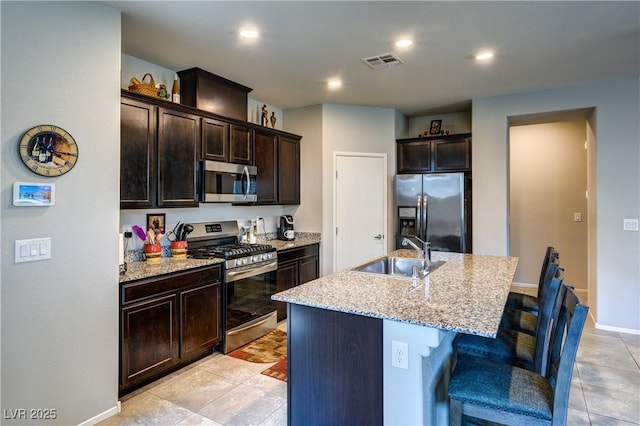 5854 Olivine Falls Ave, Las Vegas, NV 89130 - kitchen featuring appliances with stainless steel finishes, a sink, dark brown cabinetry, a center island with sink, and a breakfast bar