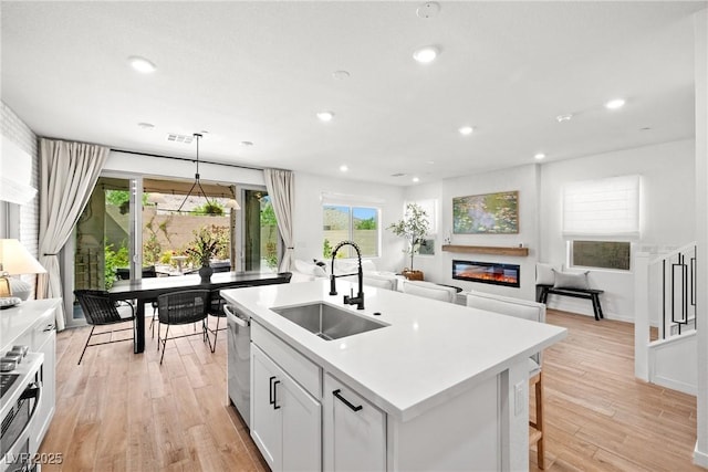 11652 Desert Hollow Ave, Las Vegas, NV 89138 - kitchen featuring a sink, dishwasher, light wood finished floors, a glass covered fireplace, and an island with sink