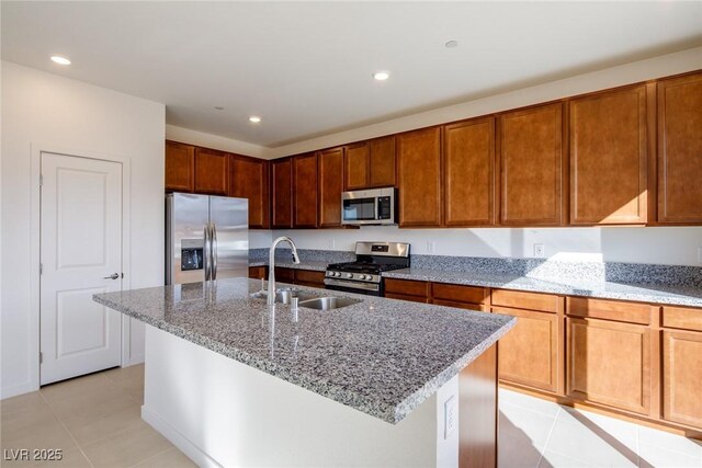 89 Via Franello, Henderson, NV 89011 - kitchen featuring appliances with stainless steel finishes, a sink, light tile patterned flooring, light stone counters, and a center island with sink