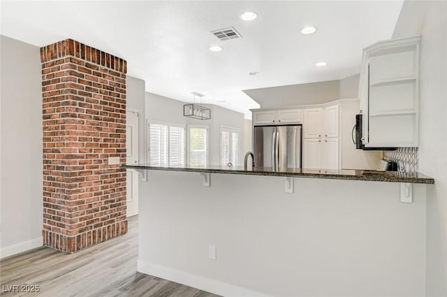 5931 Allanche Ave, Las Vegas, NV 89141 - kitchen featuring freestanding refrigerator, dark stone countertops, white cabinetry, a breakfast bar, and a peninsula
