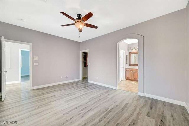 5931 Allanche Ave, Las Vegas, NV 89141 - unfurnished bedroom featuring light wood finished floors, arched walkways, connected bathroom, a walk in closet, and ceiling fan