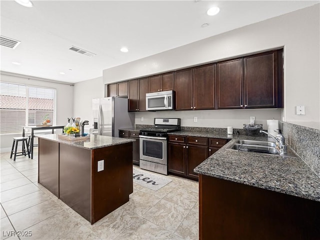 4563 Townwall St, Las Vegas, NV 89115 - kitchen with stainless steel appliances, a sink, a kitchen island, dark stone counters, and dark brown cabinetry