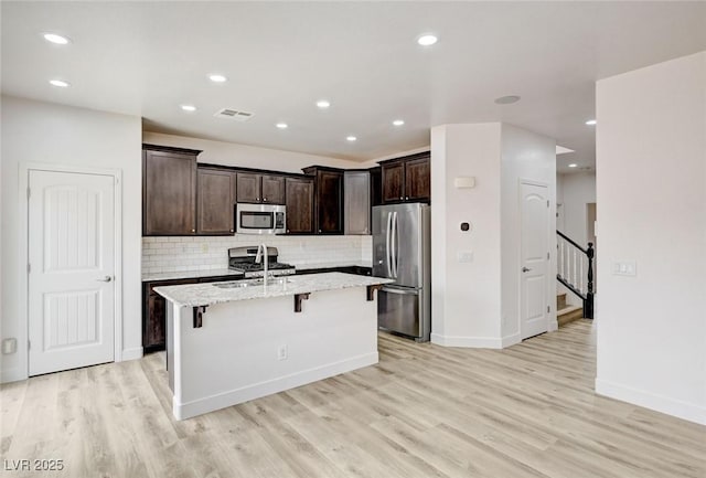 7372 S Palo Real Ct, Las Vegas, NV 89179 - kitchen with appliances with stainless steel finishes, a kitchen bar, light wood-style flooring, a center island with sink, and recessed lighting