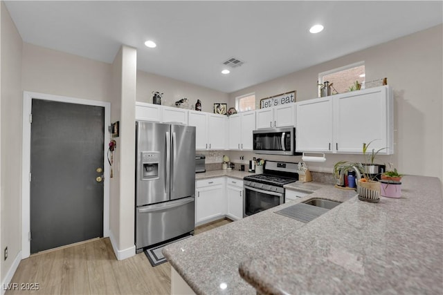 6108 Shallow Springs St, Las Vegas, NV 89130 - kitchen with stainless steel appliances, white cabinets, light wood-style floors, a sink, and light stone counters