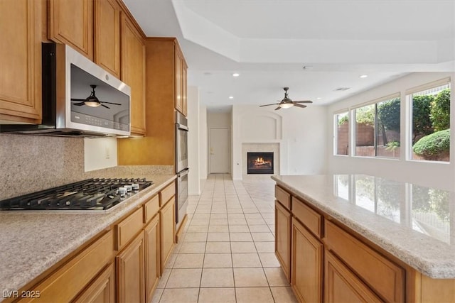 10680 Sapphire Vista Ave, Las Vegas, NV 89144 - kitchen with appliances with stainless steel finishes, a ceiling fan, a lit fireplace, light tile patterned floors, and recessed lighting