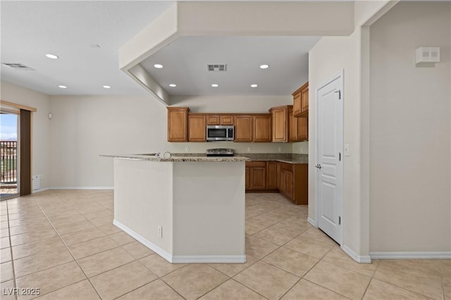 1407 Wheelwright Ct, Mesquite, NV 89034 - kitchen with stainless steel microwave, light tile patterned floors, brown cabinetry, recessed lighting, and range with electric stovetop