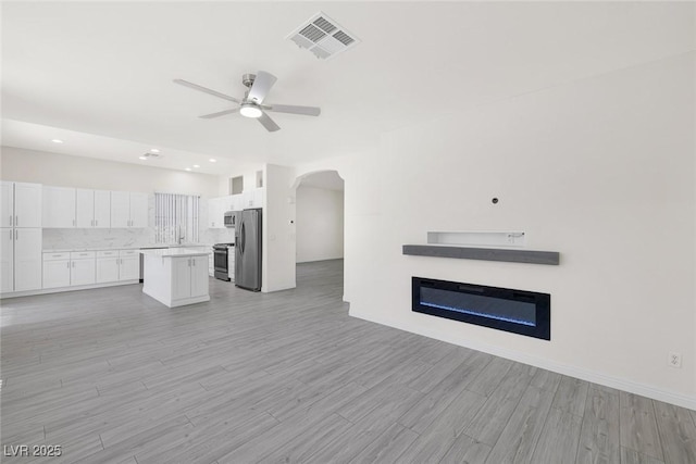2367 Tilden Way, Henderson, NV 89074 - unfurnished living room featuring ceiling fan, light wood finished floors, arched walkways, a glass covered fireplace, and recessed lighting
