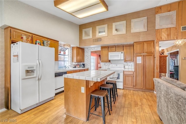 6508 Peppermill Dr, Las Vegas, NV 89146 - kitchen with white appliances, tile counters, a kitchen island, light wood-type flooring, and a towering ceiling