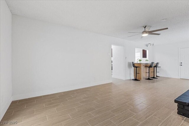 2408 Berkley Ave, Las Vegas, NV 89101 - unfurnished living room featuring a bar, light wood-style flooring, a ceiling fan, a textured ceiling, and baseboards