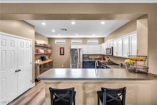 7029 Bocaire Dr, Las Vegas, NV 89131 - kitchen with stainless steel appliances, white cabinets, light wood-style floors, a peninsula, and a kitchen breakfast bar