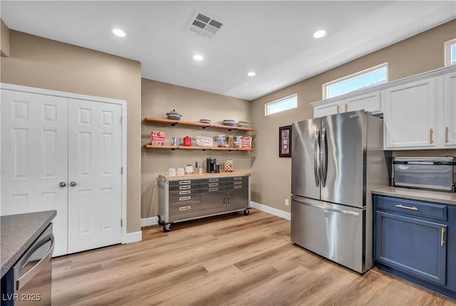 7029 Bocaire Dr, Las Vegas, NV 89131 - kitchen with stainless steel appliances, blue cabinetry, white cabinets, baseboards, and light wood finished floors