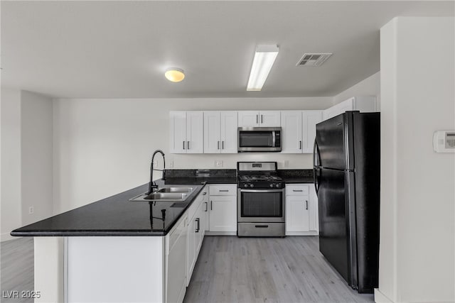 6117 Daisy Lee Ave, Las Vegas, NV 89108 - kitchen with stainless steel appliances, a sink, a peninsula, light wood-style flooring, and dark countertops