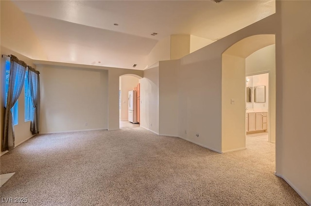 3426 Side Saddle Ct, North Las Vegas, NV 89032 - empty room featuring arched walkways, light colored carpet, vaulted ceiling, and baseboards