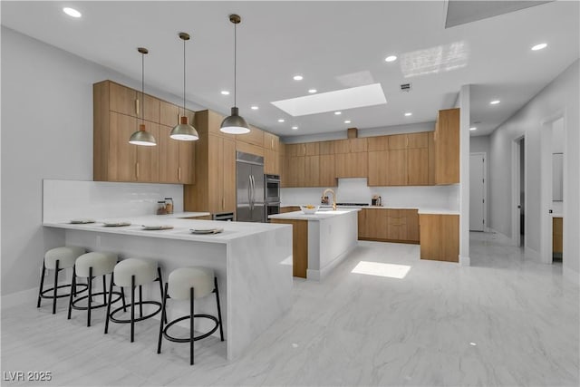 7738 Willow Cove Cir, Las Vegas, NV 89129 - kitchen featuring modern cabinets, appliances with stainless steel finishes, a skylight, brown cabinets, and a center island with sink