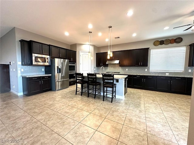 10719 Hammett Park Ave, Las Vegas, NV 89166 - kitchen featuring stainless steel appliances, tasteful backsplash, under cabinet range hood, a breakfast bar, and light tile patterned floors