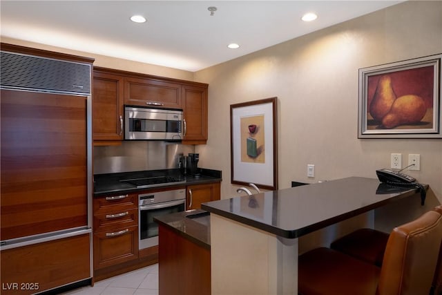145 E Harmon Ave Unit 1120, Las Vegas, NV 89109 - kitchen featuring appliances with stainless steel finishes, dark countertops, a peninsula, brown cabinetry, and a breakfast bar