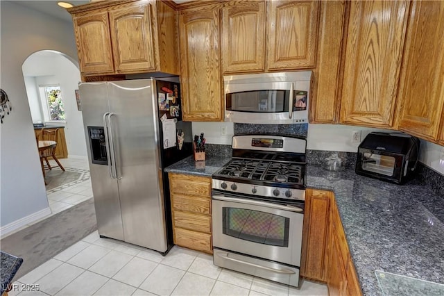 3451 Sagebrush Ave, Pahrump, NV 89048 - kitchen featuring stainless steel appliances, light tile patterned flooring, arched walkways, and brown cabinets