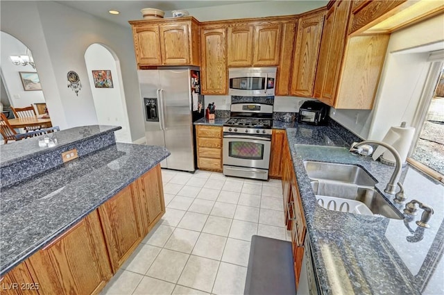 3451 Sagebrush Ave, Pahrump, NV 89048 - kitchen with appliances with stainless steel finishes, a sink, arched walkways, dark stone countertops, and light tile patterned flooring