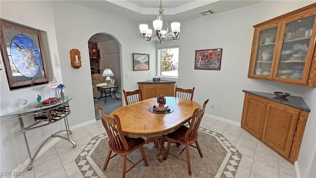 3451 Sagebrush Ave, Pahrump, NV 89048 - dining room with light tile patterned floors, arched walkways, baseboards, inlaid floor details, and a tray ceiling