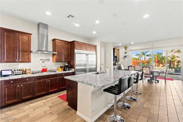 6980 W Meranto Ave, Las Vegas, NV 89178 - kitchen with appliances with stainless steel finishes, wall chimney range hood, light wood-style flooring, an island with sink, and a kitchen bar