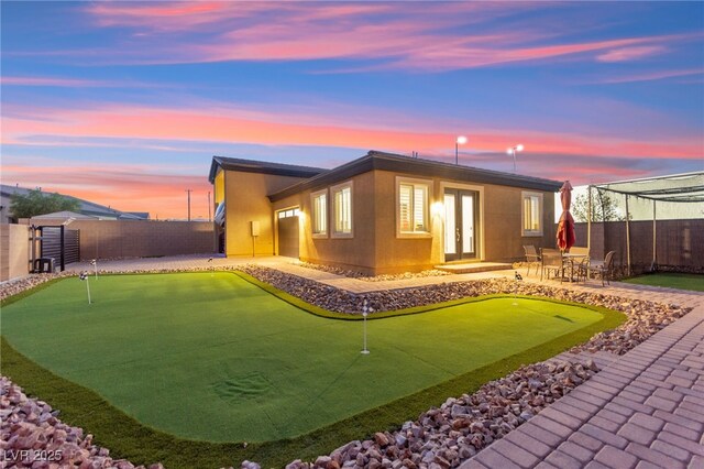 6980 W Meranto Ave, Las Vegas, NV 89178 - back of property at dusk featuring an area to practice putting, a fenced backyard, a patio area, and french doors