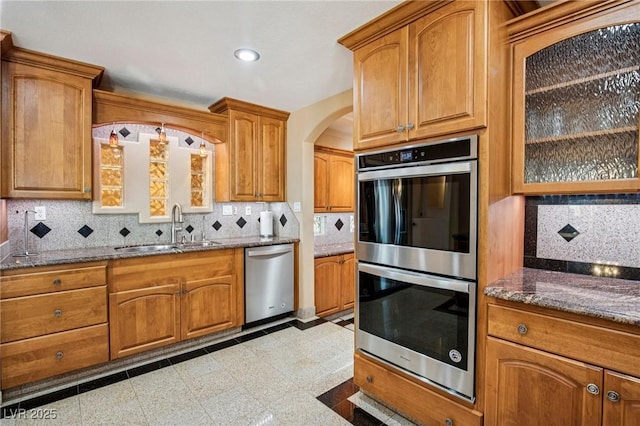 9111 W Stephen Ave, Las Vegas, NV 89149 - kitchen featuring appliances with stainless steel finishes, a sink, dark stone countertops, arched walkways, and brown cabinets