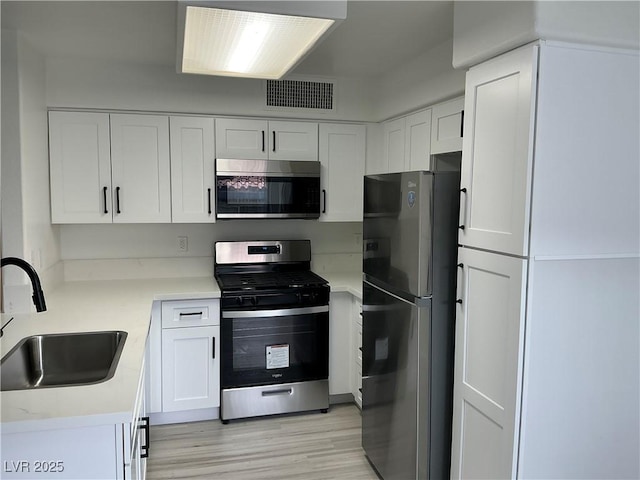 5222 Mandalay Springs Dr Unit 202, Las Vegas, NV 89120 - kitchen featuring appliances with stainless steel finishes, a sink, white cabinets, light wood finished floors, and light countertops