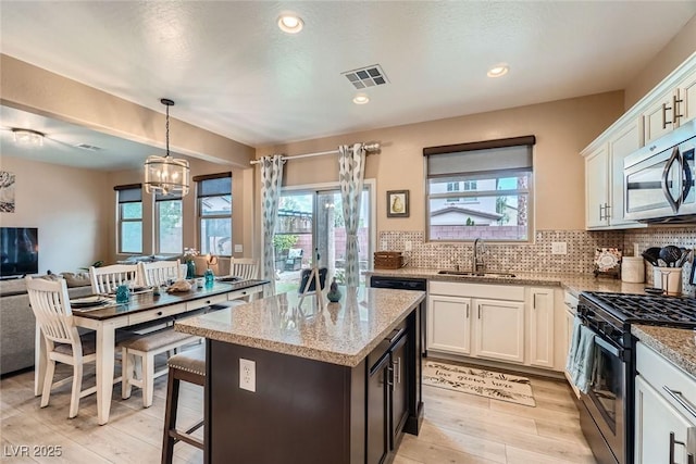 9853 Bangalore Ct, Las Vegas, NV 89148 - kitchen featuring appliances with stainless steel finishes, a sink, white cabinets, light wood-type flooring, and light stone countertops