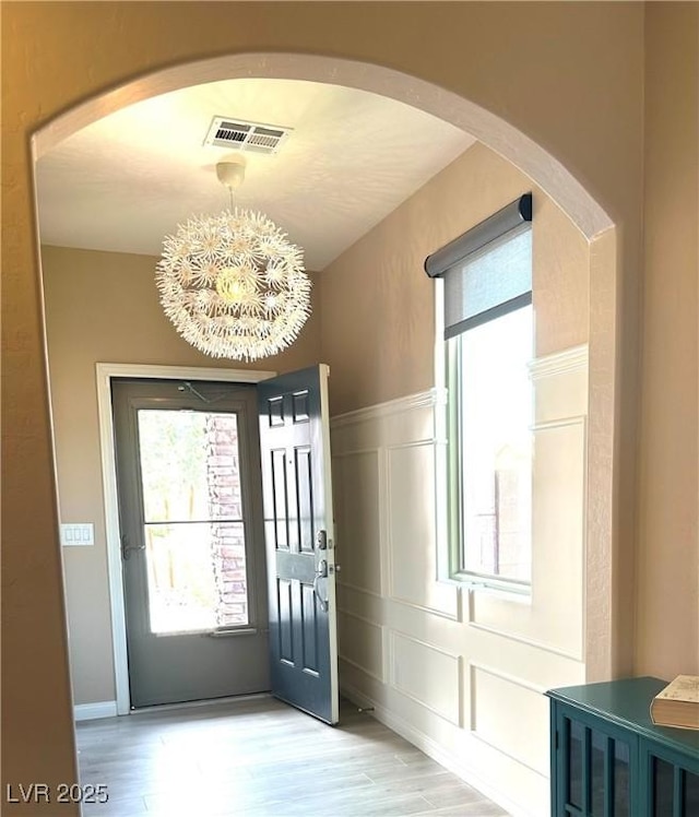 9853 Bangalore Ct, Las Vegas, NV 89148 - foyer entrance featuring a decorative wall, a chandelier, light wood-type flooring, wainscoting, and arched walkways