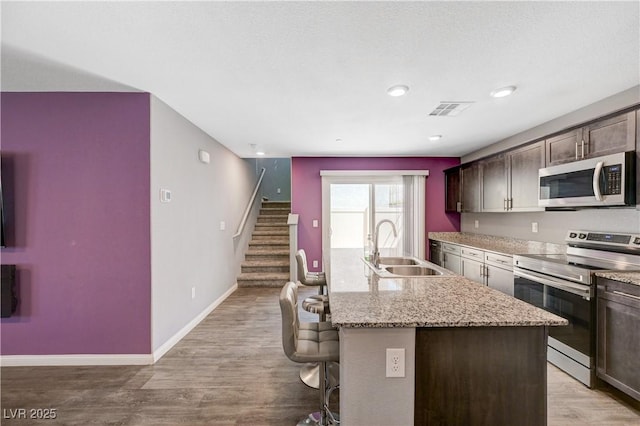 6940 Crescent Gold St, North Las Vegas, NV 89086 - kitchen with appliances with stainless steel finishes, a sink, a breakfast bar, dark brown cabinets, and an island with sink
